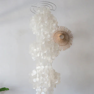 Handmade seashell chandelier with cascading white shells and rattan detail against white wall
