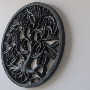 Hand-carved black wood wall art with intricate tree of life design on a white wall