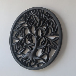 Hand-carved black wood wall art featuring a round tree of life design on a white wall.