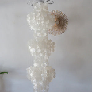 Large white seashell chandelier with round capiz shells, hanging against a plain wall
