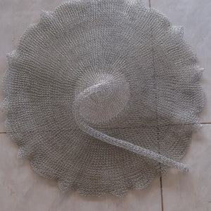 Handwoven silver wire wall decor with scalloped edges on tiled floor