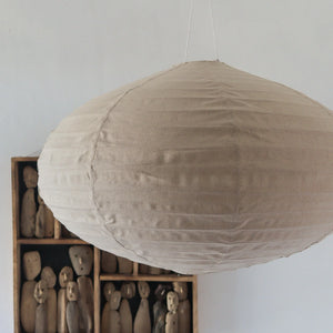 Handmade beige linen pendant lamp with wooden carved figurines in background