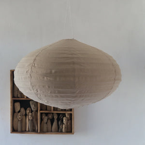 Natural fabric pendant lampshade hanging above wooden artisanal figurines on white wall