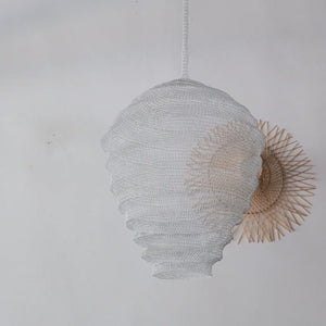 Handwoven white rattan pendant lamp with a unique sculpted shape against a neutral wall
