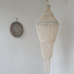 Handmade Balinese seashell chandelier with intricate design hanging on white wall