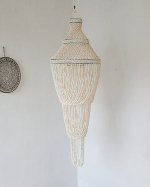 Handcrafted Balinese seashell chandelier with intricate beaded design hanging on white wall