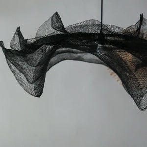 Handmade black mesh pendant light with flowing, artistic design on a neutral background