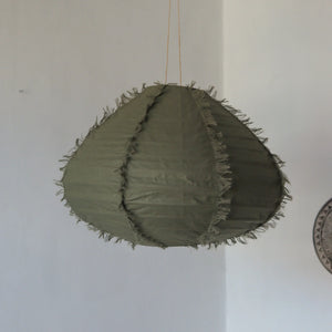 Green fabric pendant lamp with fringe details, hanging in a minimalist room