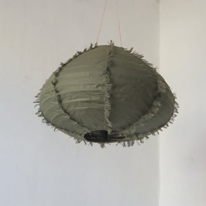 Handmade olive green fabric pendant light with frayed edges hanging in a minimalist room