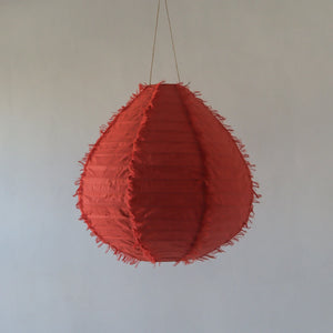 Handmade red fabric pendant lamp with textured fringe, hanging against a neutral wall