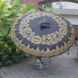 Large black and gold Balinese decorative umbrella with intricate floral patterns outdoors