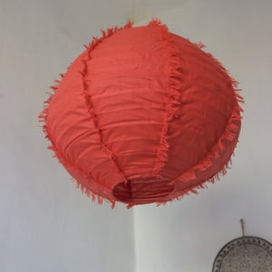 Handmade red fabric lantern with frayed seams, hanging in a minimalist interior setting.