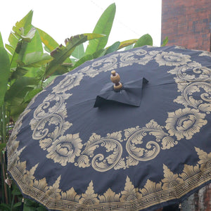 Balinese umbrella with ornate gold patterns outdoors, tropical leaves in background