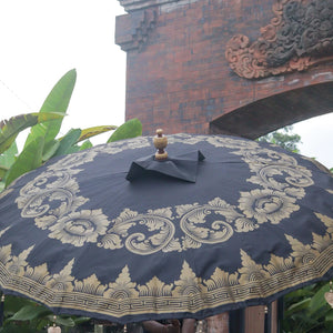 Balinese decorative umbrella with gold patterns, outdoor temple gate and greenery