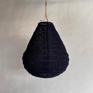 Handmade black woven pendant light with teardrop shape hanging against a neutral wall
