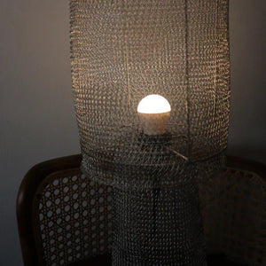 Handmade woven mesh lampshade with glowing bulb, rattan chair in background
