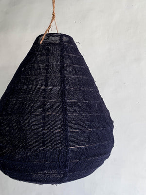 Handwoven black pendant lamp shade with natural fiber texture, hanging against a white wall