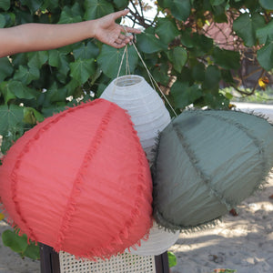 Handmade Balinese fabric lanterns in red, green, and white, displayed outdoors with tropical leaves.