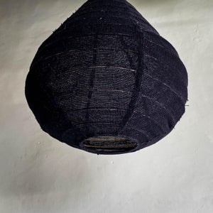 Handmade black woven pendant lamp shade against a neutral wall, eco-friendly home decor