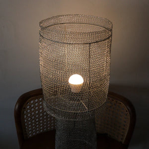 Handmade mesh metal table lamp with warm light, rattan chair in background, modern decor