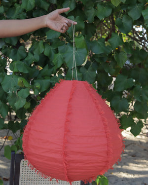 Hand holding a red fabric hanging lamp with fringe, outdoor leafy background