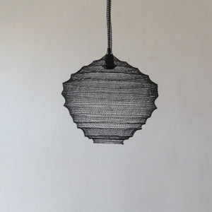 Handmade black mesh pendant light with sculptural design against a neutral wall