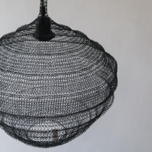 Handcrafted black wire pendant light with intricate mesh design against a plain wall