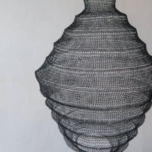 Handwoven black wire pendant light with organic, layered shape against a white wall
