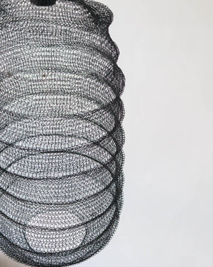 Handcrafted black wire mesh pendant light with a spiral design against a white background.