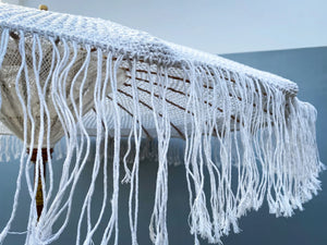 Handmade Balinese white macrame umbrella with fringe detail against a blue background