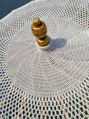 Handcrafted Balinese white crochet parasol with carved golden wooden finial outdoors.