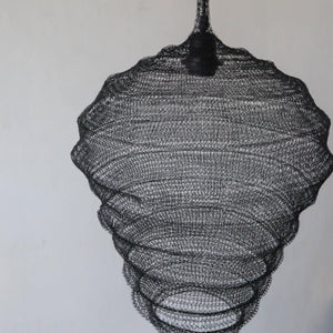 Handwoven black rattan pendant light with intricate layered design against a plain wall