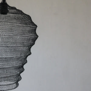 Handmade black wire mesh pendant light with organic shape against a neutral wall.