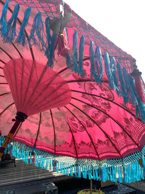 Handmade Balinese umbrella in vibrant pink with blue tassels, showcasing intricate design and craftsmanship.