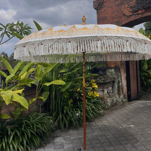 Balinese decorative umbrella with gold pattern and fringe in a tropical outdoor garden setting