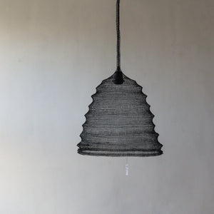 Handmade black woven pendant light against a plain wall, modern boho home decor