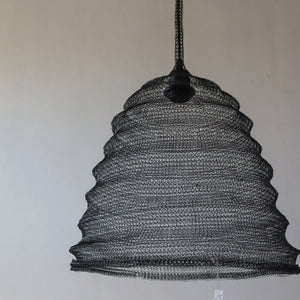Handwoven black wire pendant light with a wavy dome shape against a neutral wall