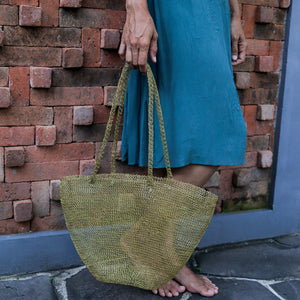 Hand holding woven natural fiber tote bag, woman in blue dress by brick wall