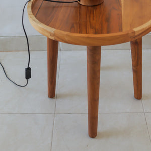 Handcrafted round teak wood table with three legs on a tiled floor