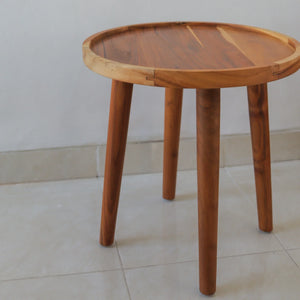 Handmade wooden round side table with natural finish and three legs on tiled floor