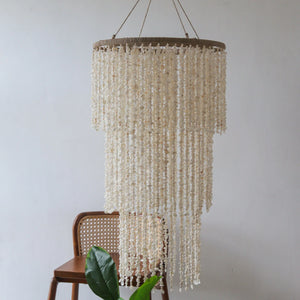 Handcrafted Balinese seashell chandelier hanging above a wooden chair and green plant