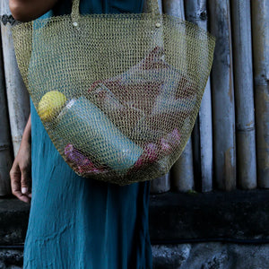 Eco-friendly mesh tote bag with groceries, woman in teal dress by bamboo wall