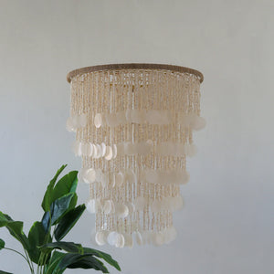 Handmade seashell chandelier with cascading white shells, natural decor above green plant