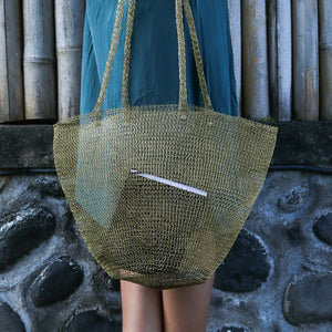Handwoven eco-friendly straw tote bag held against a stone and bamboo background