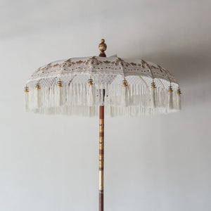 Hand painted Balinese parasol in white, featuring intricate designs and fringed edges, perfect for decor.