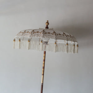Hand painted white Balinese parasol with intricate gold motifs and fringed edge, showcasing artisan craftsmanship.