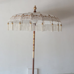 Hand painted Balinese parasol in white with intricate gold motifs and fringe, perfect for decor.
