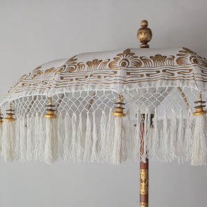 Hand-painted Balinese parasol in white with gold motifs and fringes, showcasing intricate craftsmanship.