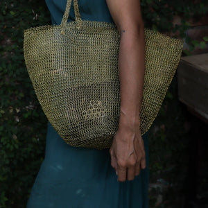 Hand holding natural woven tote bag, eco-friendly craftsmanship, green dress in background