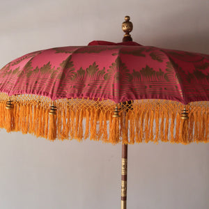 Balinese decorative umbrella with pink and gold fabric, wooden pole, and yellow fringe tassels